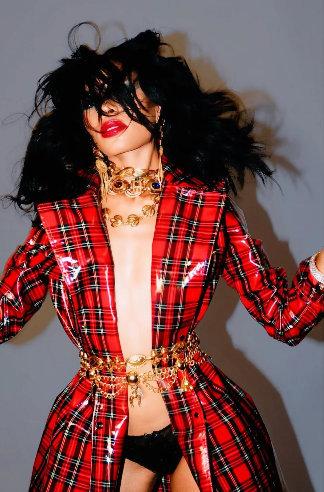 High-gloss red tartan vinyl coat worn open with layered gold chains